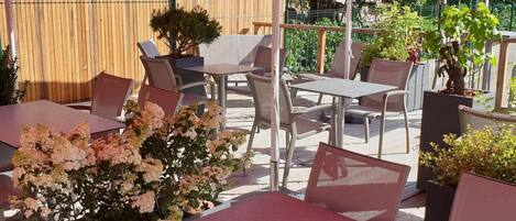 An outdoor patio area with tables and chairs, surrounded by potted plants and a wooden fence.