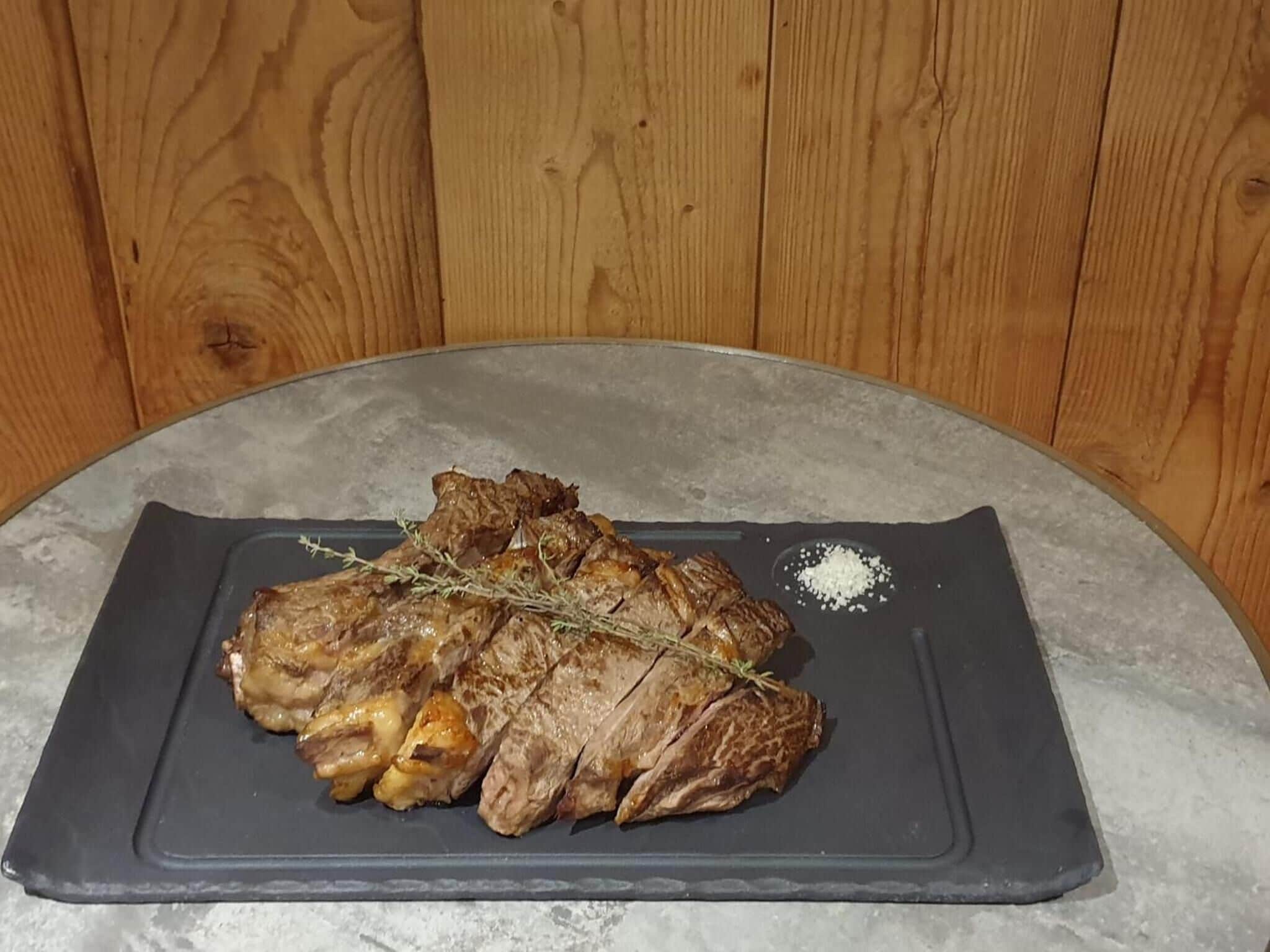 A plate of grilled meat with a sprig of thyme and salt on a dark plate.
