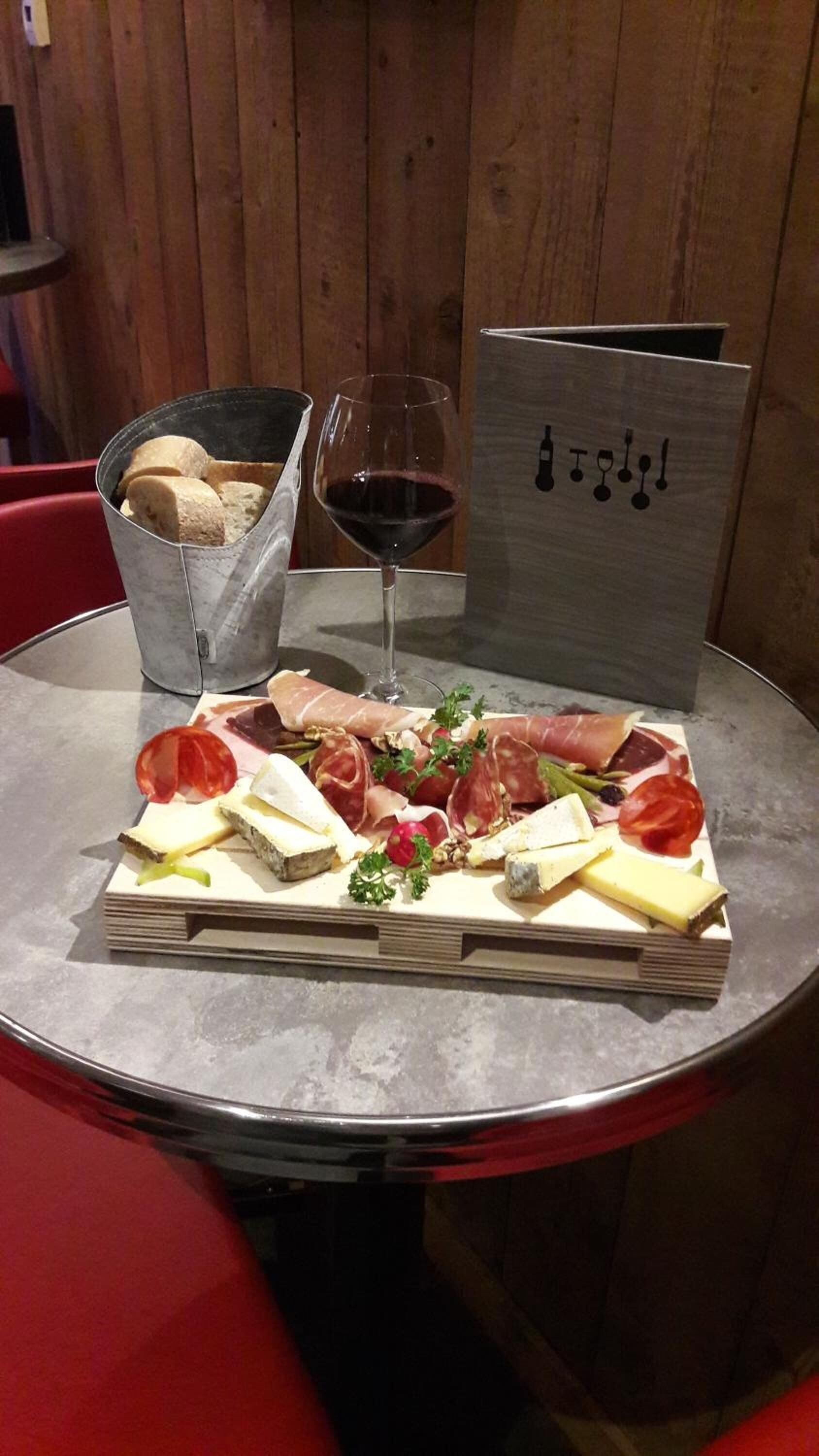 Una tabla de quesos y embutidos con diversos tipos de carne, queso y una copa de vino tinto sobre una mesa.