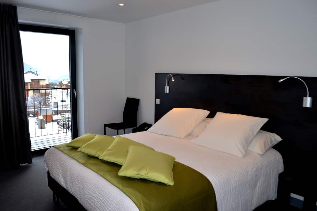 Moderni hotellihuone, jossa on suuri sänky, näkymä parvekeovesta ja musta pääty.