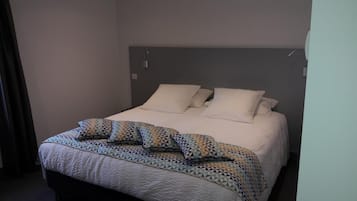 Una cama bien hecha con un edredón estampado y almohadas, un cabecero sencillo y un diseño de habitación limpio y despejado.