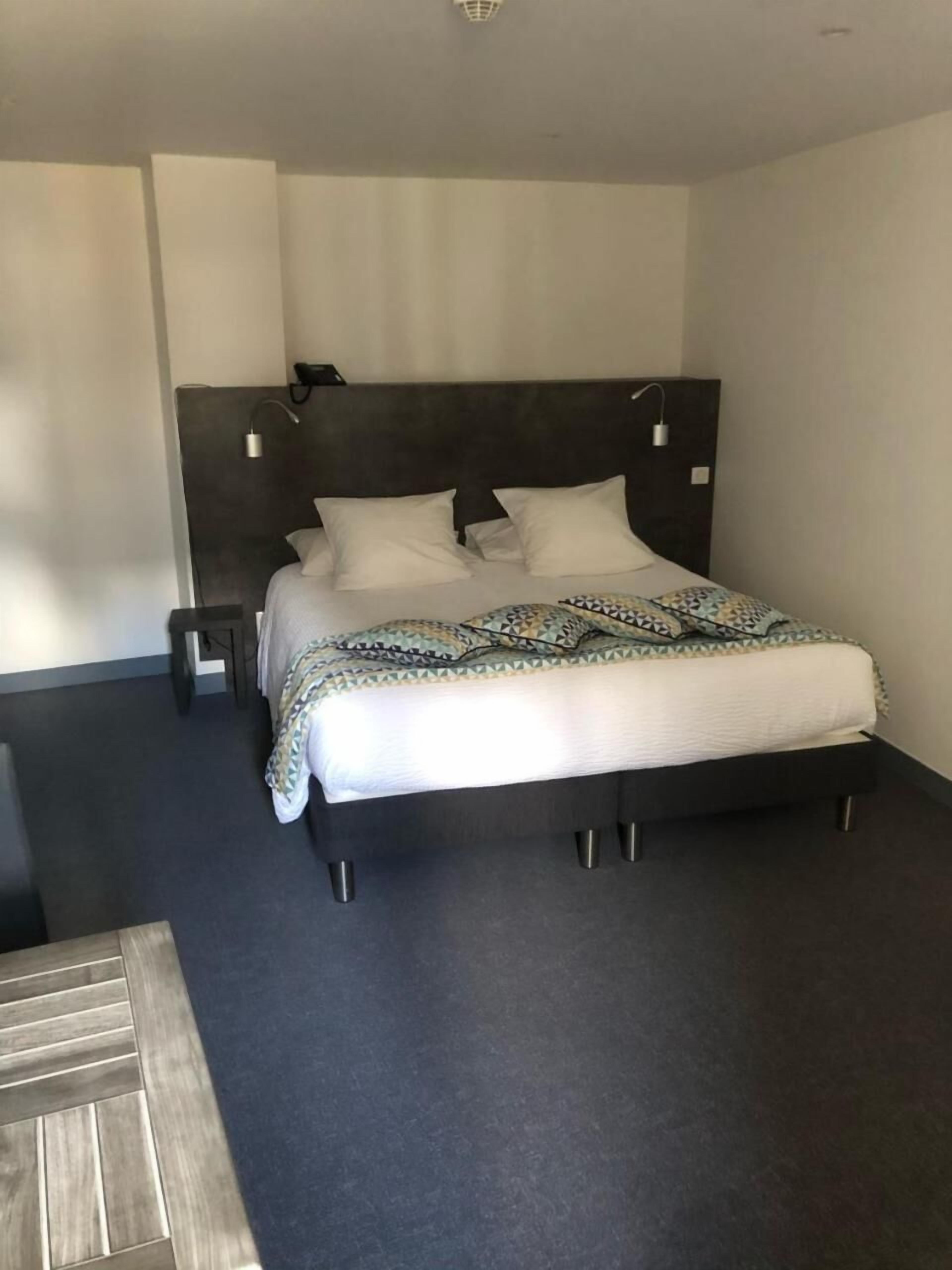 Un dormitorio moderno con cabecera oscura, una cama grande con ropa de cama estampada y una mesita de noche pequeña.