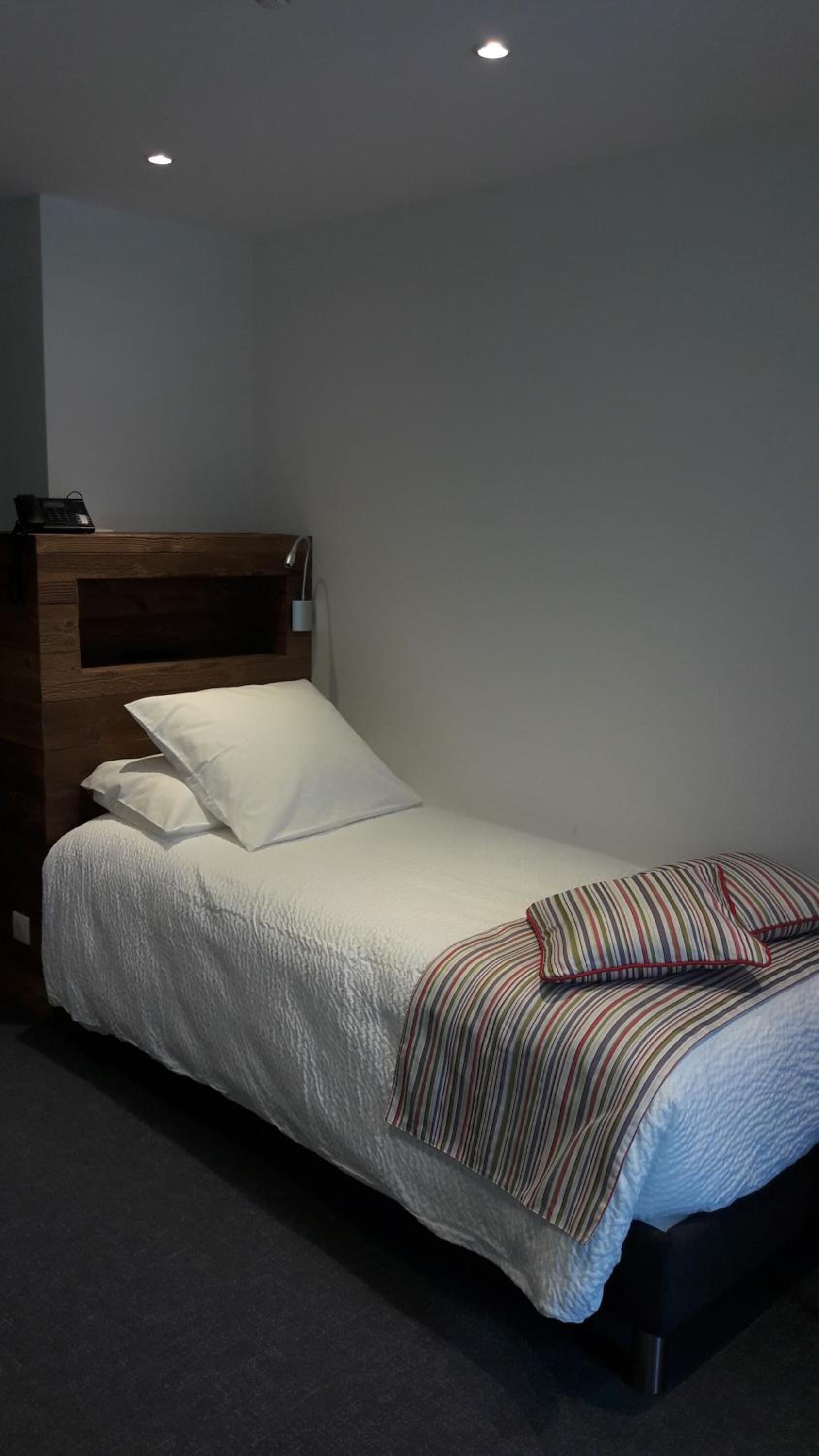A single bed with a wooden headboard, white bedding, and striped pillows.