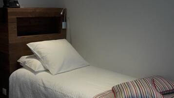 A single bed with a wooden headboard, white bedding, and striped pillows.