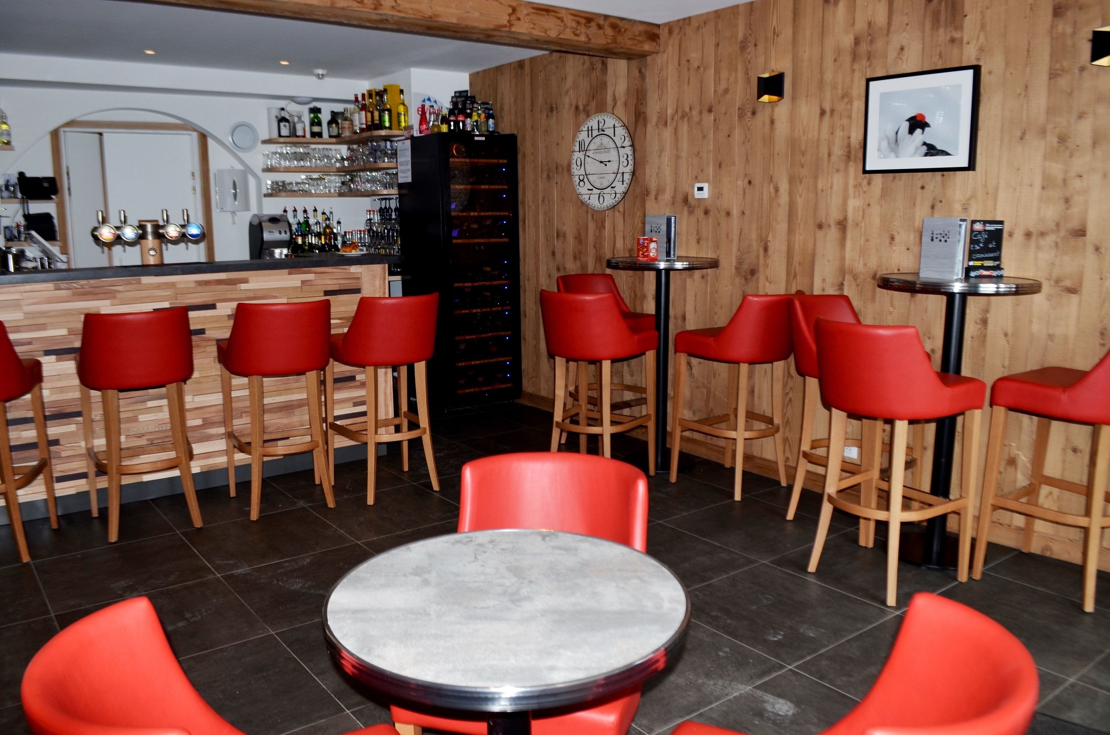 A bar area with red bar stools, a round table, and a wooden wall with a clock and framed picture.