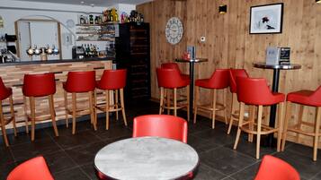 A bar area with red bar stools, a round table, and a wooden wall with a clock and framed picture.