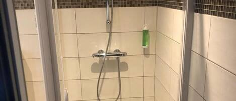 Un box de ducha con paredes de vidrio, suelo de baldosas, un cabezal de ducha manual y una botella de champú.