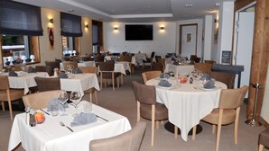Un restaurant avec de nombreuses tables dressées pour le service, chacune étant recouverte d’une nappe blanche et dotée de chaises marron.