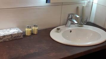 A bathroom with a white sink, dark brown countertop, and a mirror above it. There are three bottles of lotion on the counter and a stack of white towels below the mirror.