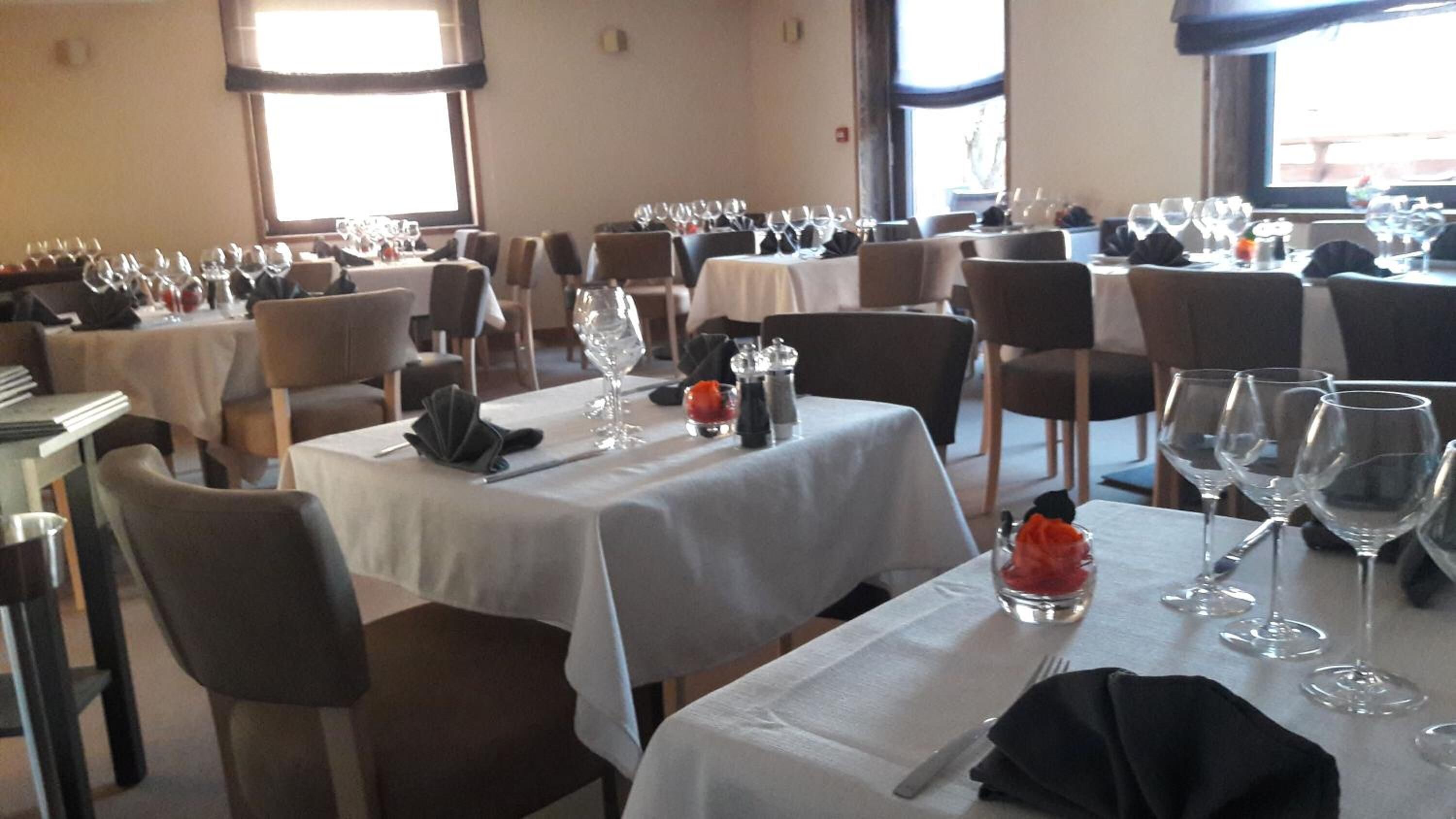 Un comedor con varias mesas dispuestas para comensales, cada una con copas de vino, cubiertos y servilletas.