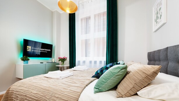 Een moderne hotelkamer met een bed, een televisie, een nachtkastje en een raam met gordijnen.