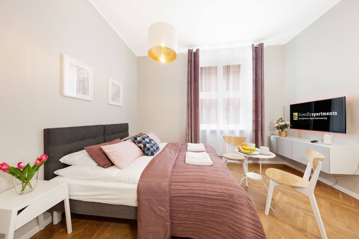 A modern bedroom with a bed, bedside table, TV, and a small desk area.