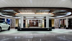 A modern hotel lobby with a central column, a white car parked outside, and a well-lit ceiling with intricate patterns. - Konark Grand Hotel (Mirzapur)