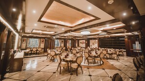 A spacious dining area with multiple tables and chairs, a central island, and a patterned floor. - Konark Grand Hotel (Mirzapur)