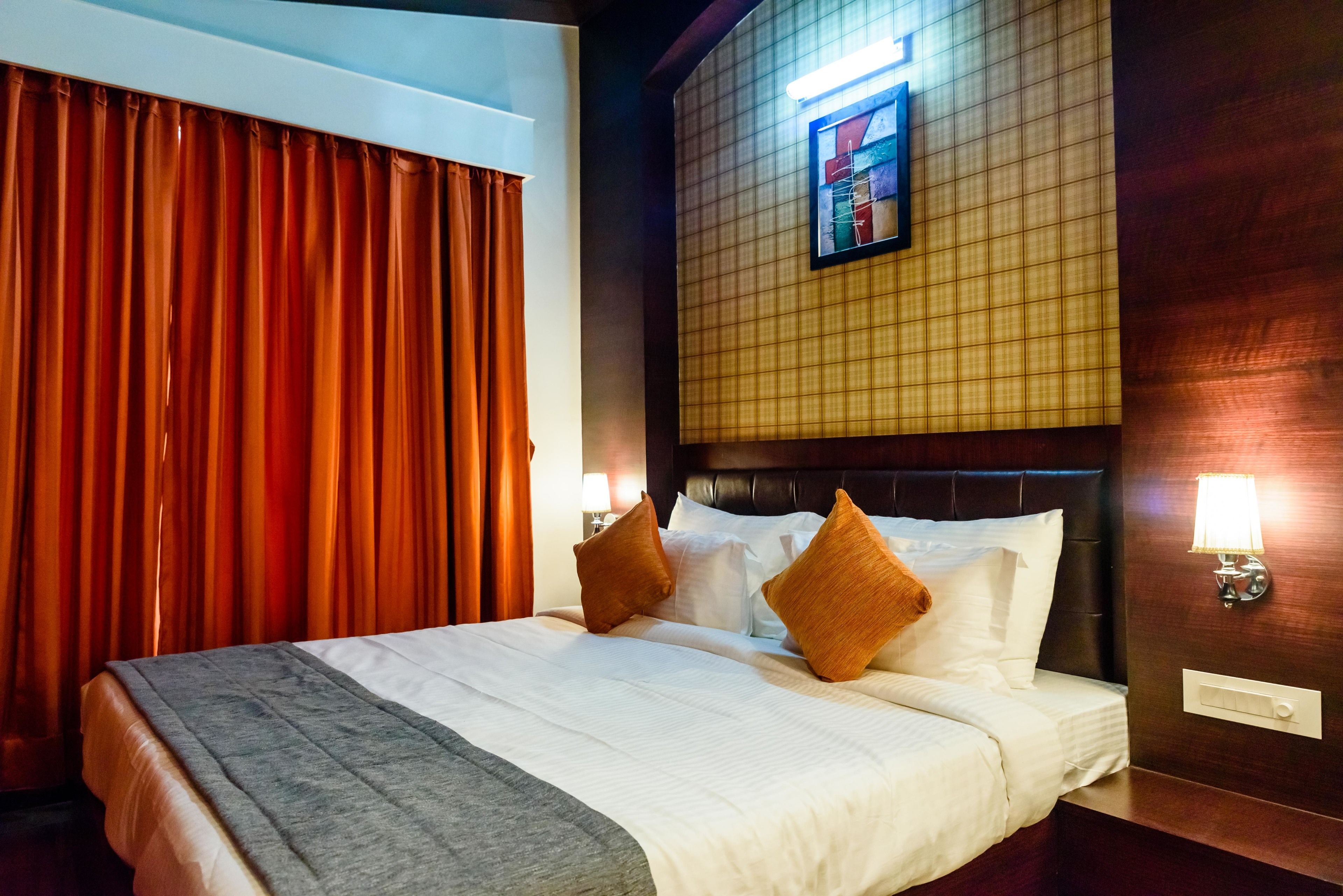 Une chambre d’hôtel avec un grand lit, des rideaux rouges, une tête de lit à motifs géométriques et des lampes fixées au mur.