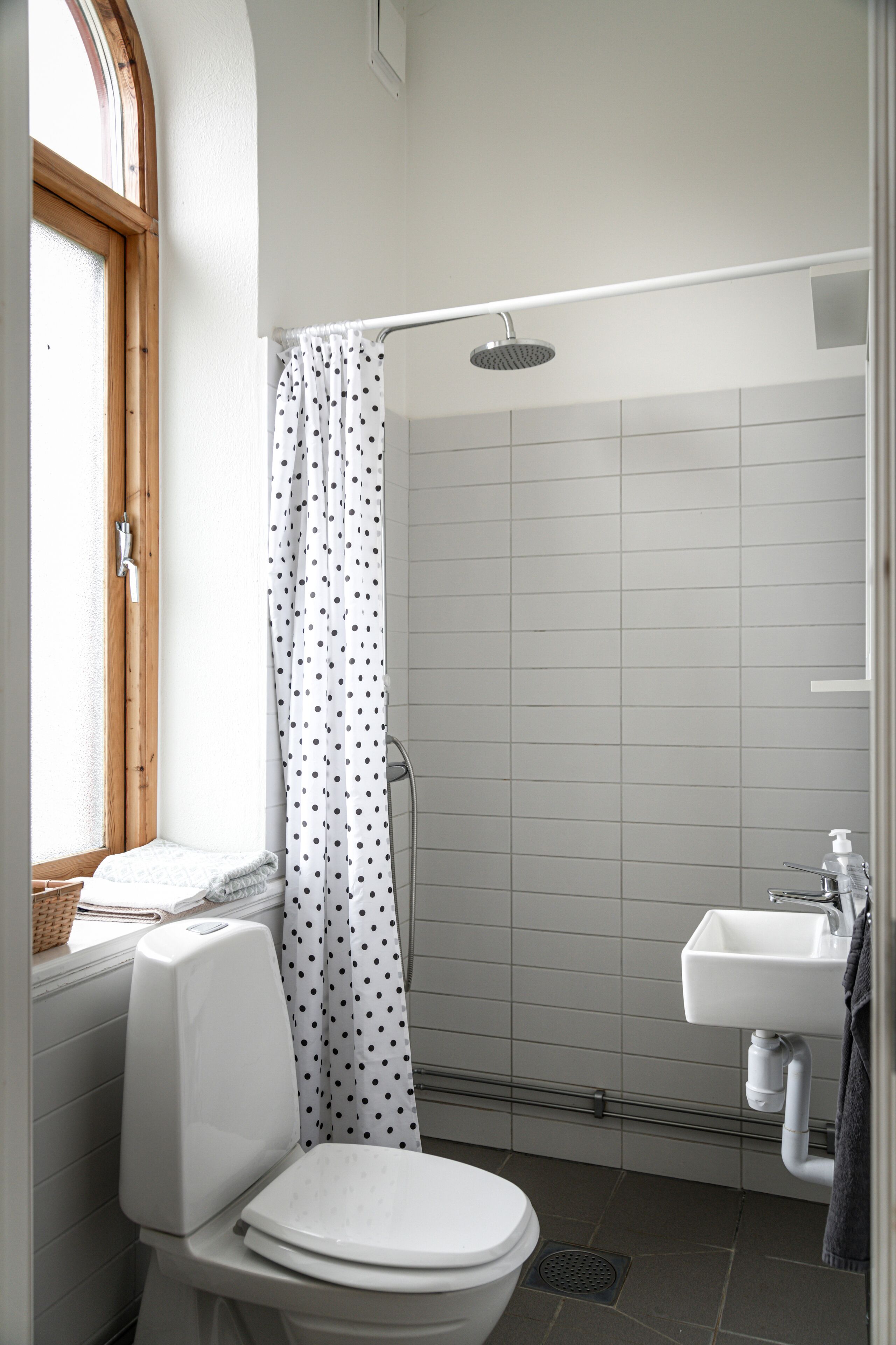 A bathroom with a toilet, a shower with a white curtain, a sink, and a window with a wooden frame.
