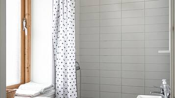A bathroom with a toilet, a shower with a white curtain, a sink, and a window with a wooden frame.