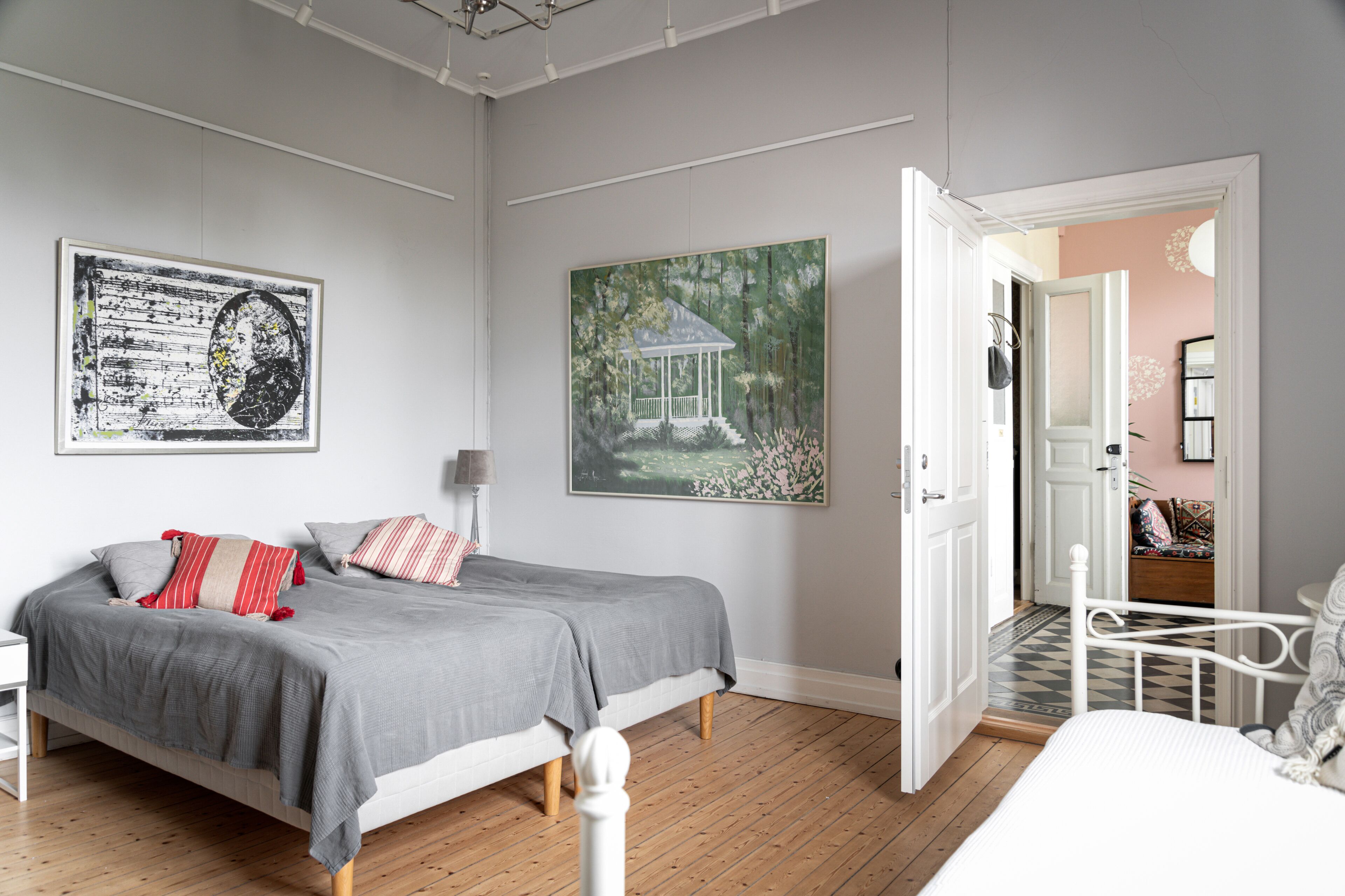 A bedroom with a bed, a nightstand, a lamp, and two paintings on the wall.