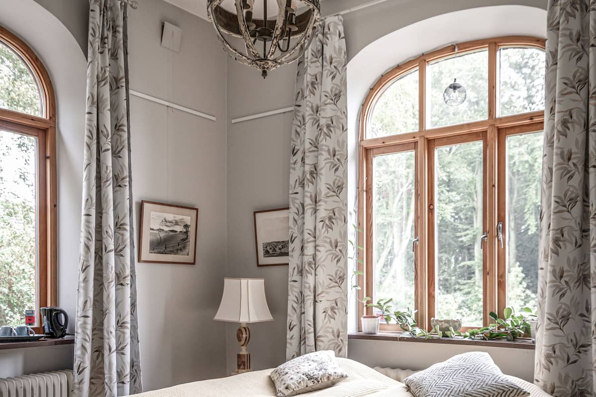 Ein Schlafzimmer mit einem großen Bett, zwei Nachttischen, einer Pendelleuchte und einem Fenster mit Vorhängen.