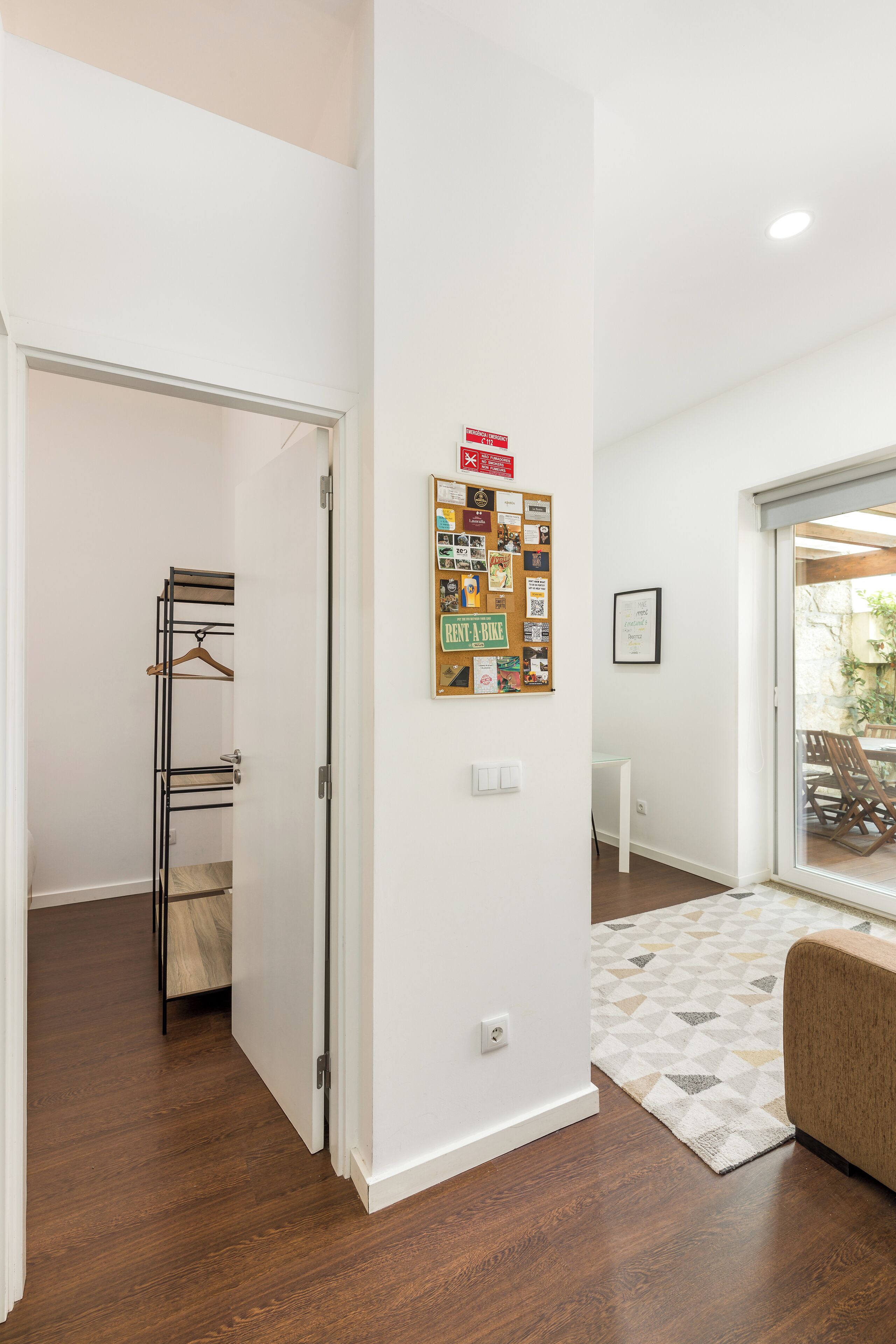 A modern interior with a wooden floor, a bulletin board, and a sliding glass door leading to an outdoor area.
