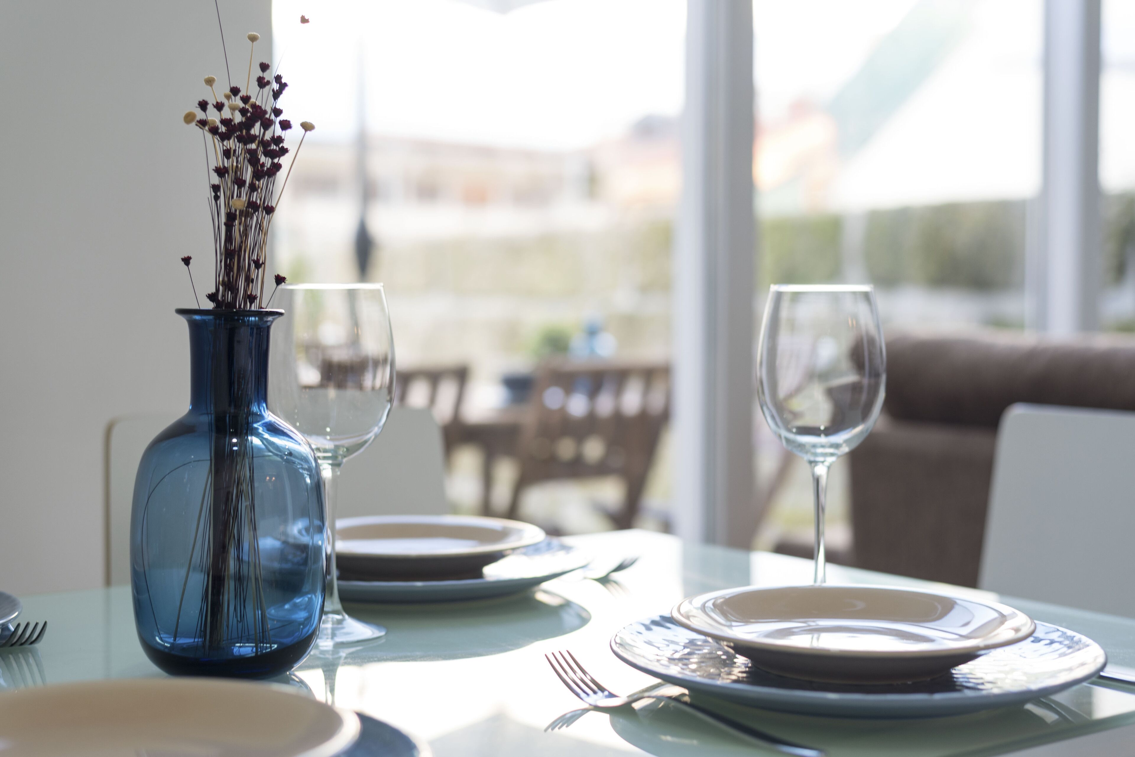 A dining table set with plates, cutlery, and a blue vase with dried flowers.