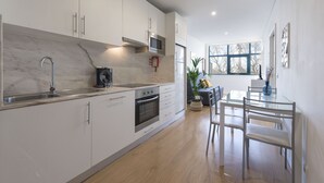 Una cucina moderna con mobili bianchi, un piano di lavoro in marmo, elettrodomestici in acciaio inossidabile e un'area pranzo con tavolo e sedie in vetro.