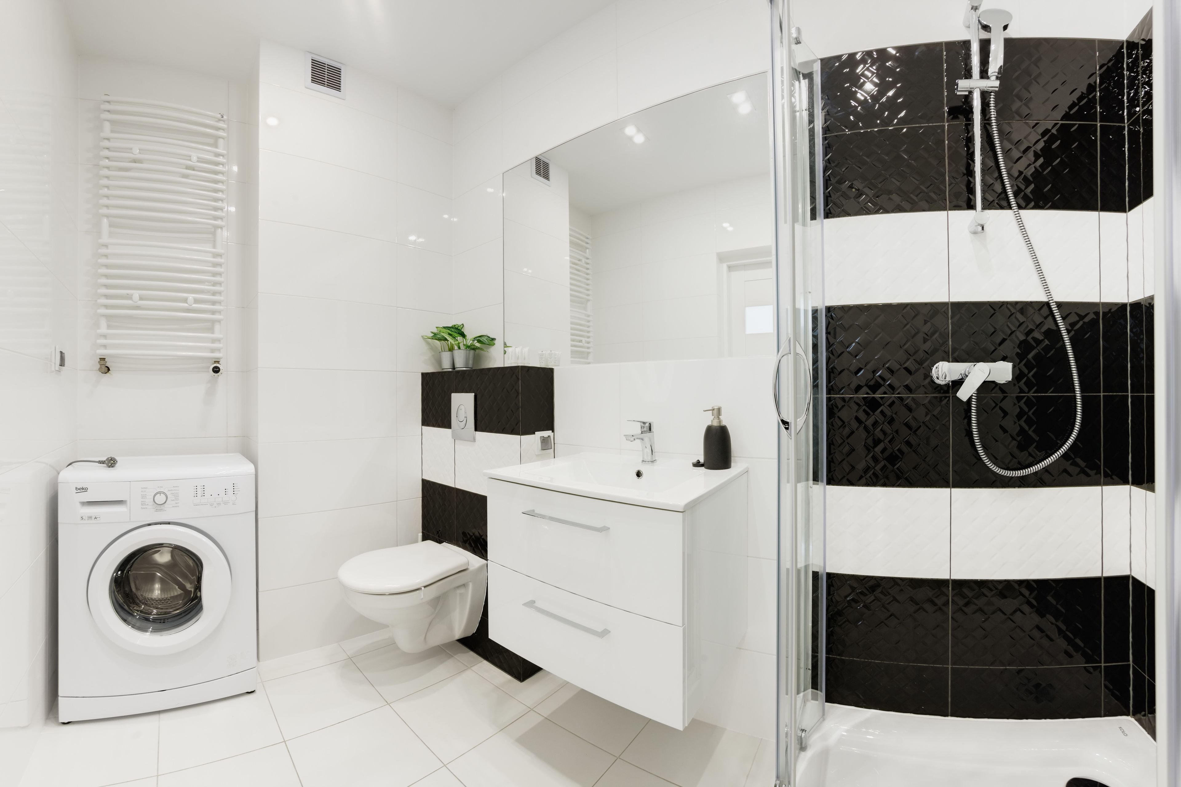 A modern bathroom with a washing machine, toilet, vanity, and a shower area.