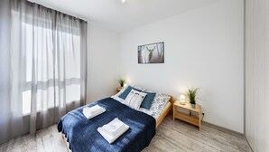 A modern bedroom with a bed, bedside tables, a ceiling fan, and a window with sheer curtains. - Friendly Apartments - Kościelna (Poznan)