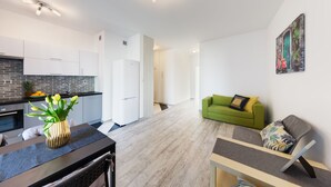 A modern kitchen with white cabinets, a black countertop, and a vase with yellow flowers. There is a green sofa with a cushion and a painting on the wall. - Friendly Apartments - Kościelna (Poznan)