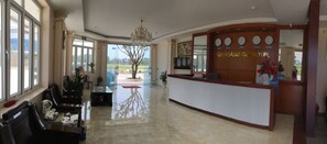 A hotel reception area with a reception desk, a chandelier, a large window, and a view of the outdoors. - Hoang Gia Hotel Thanh Hoa (Thanh Hoa)