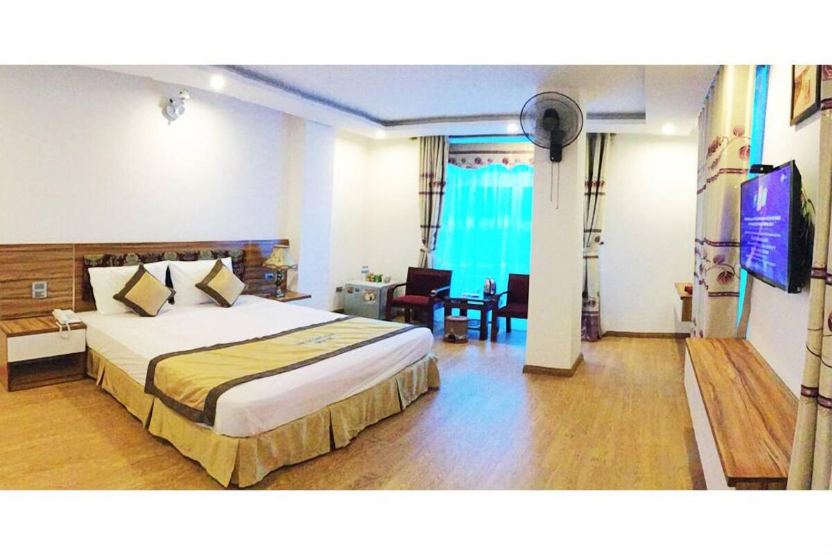 A hotel room with a large bed, bedside table, lamp, and a TV on the wall.