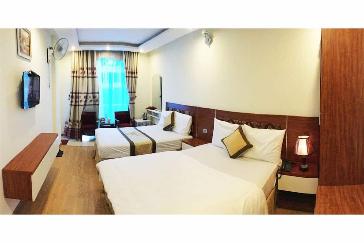A hotel room with two beds, a desk, a chair, a TV, and a window with curtains.