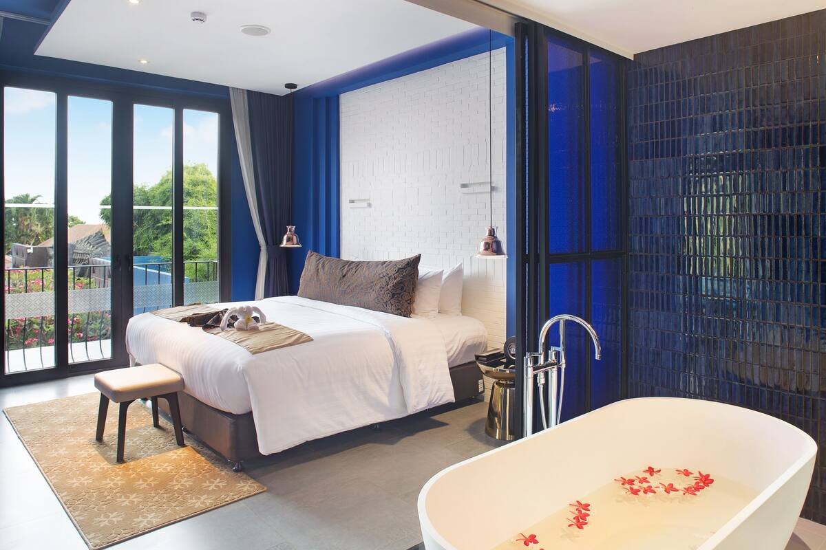 A modern bedroom with a large bed, a bathtub, and a view of the outdoors.