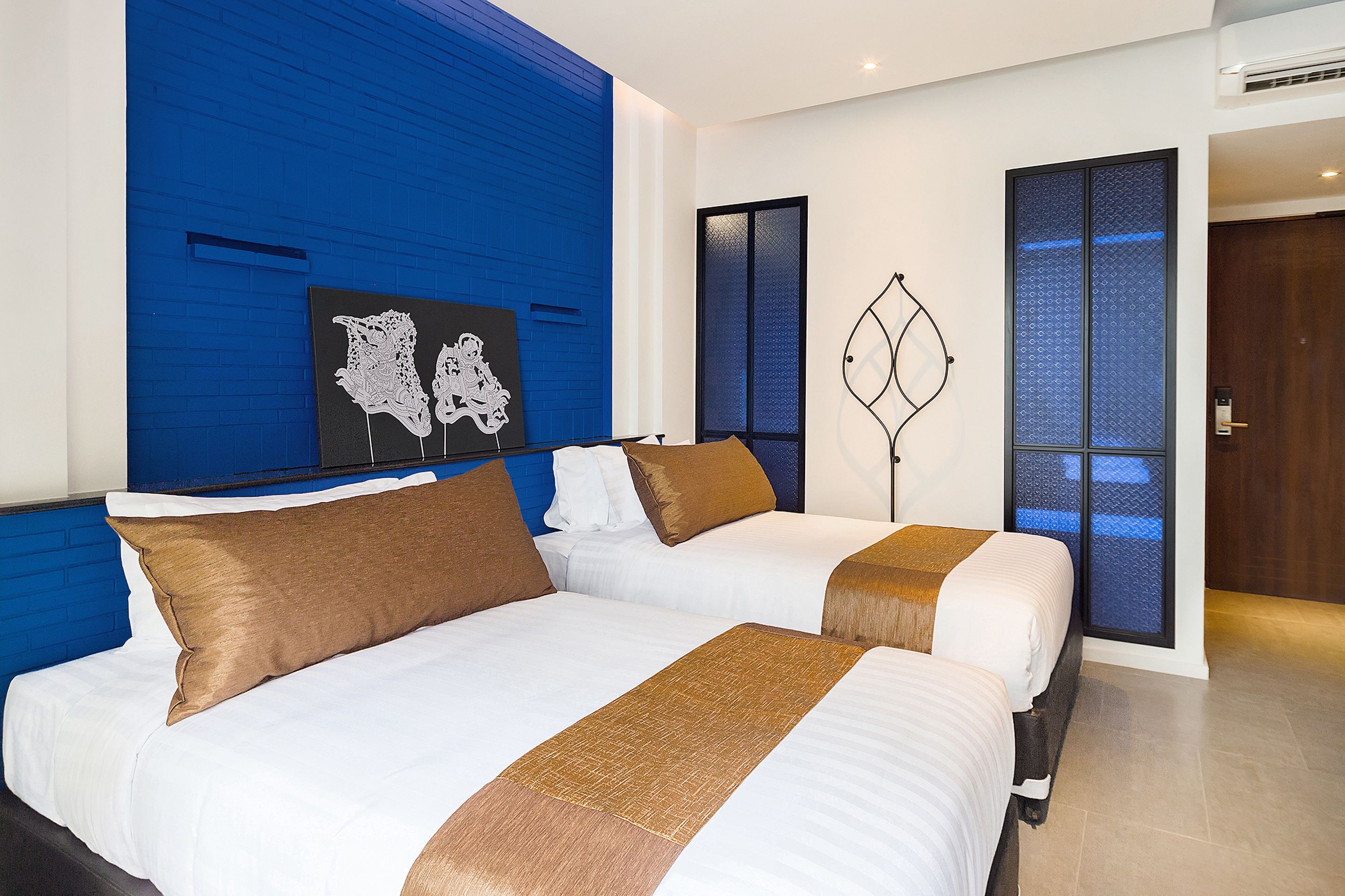 A hotel room with two beds, a blue accent wall, and artwork on the wall.