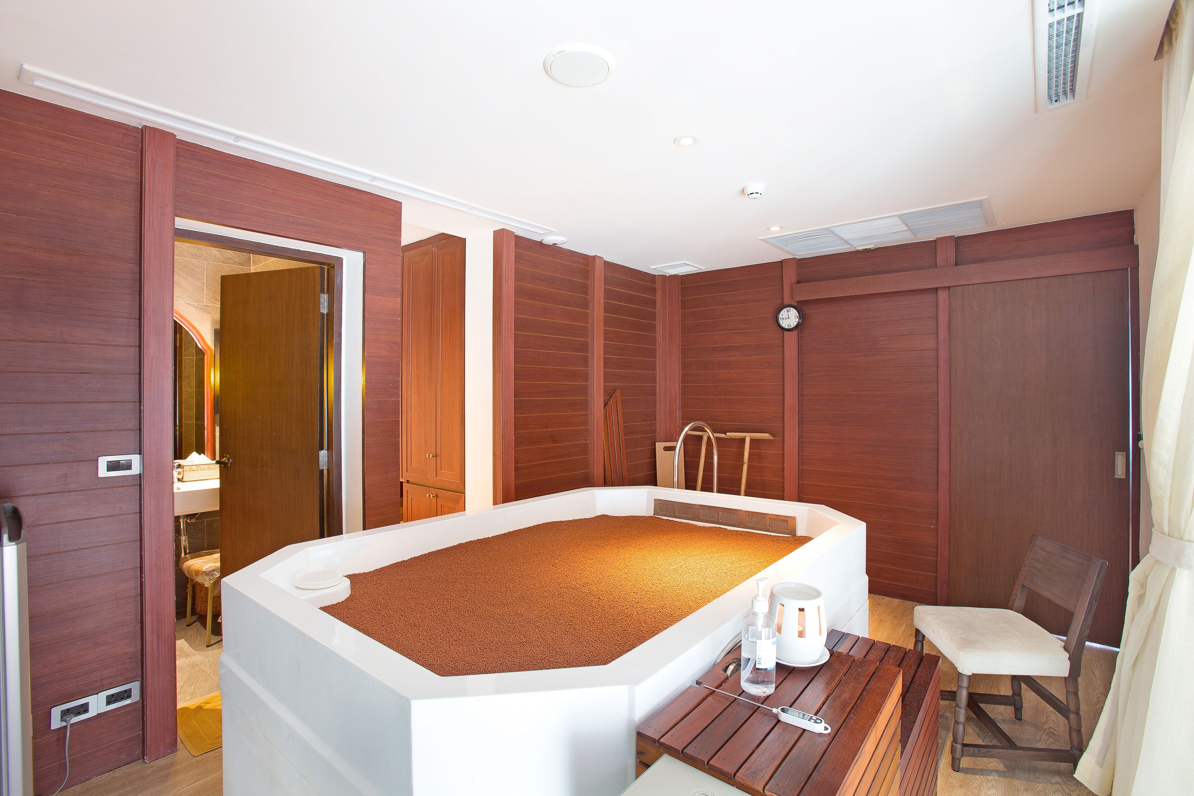 Ein Zimmer mit einer großen Badewanne, Holzwänden, einer hölzernen Bank und einem kleinen Tisch mit einer Flasche und einem Becher.