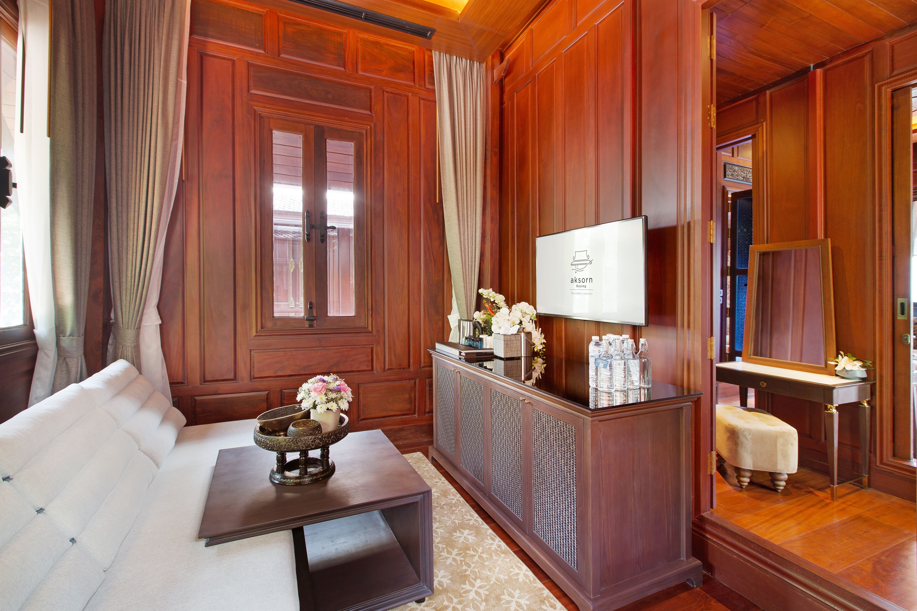 A room with a wooden paneled wall, a sofa, a small table with a vase, a mirror, and a cabinet with a television.