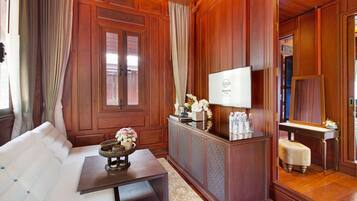 A room with a wooden paneled wall, a sofa, a small table with a vase, a mirror, and a cabinet with a television.