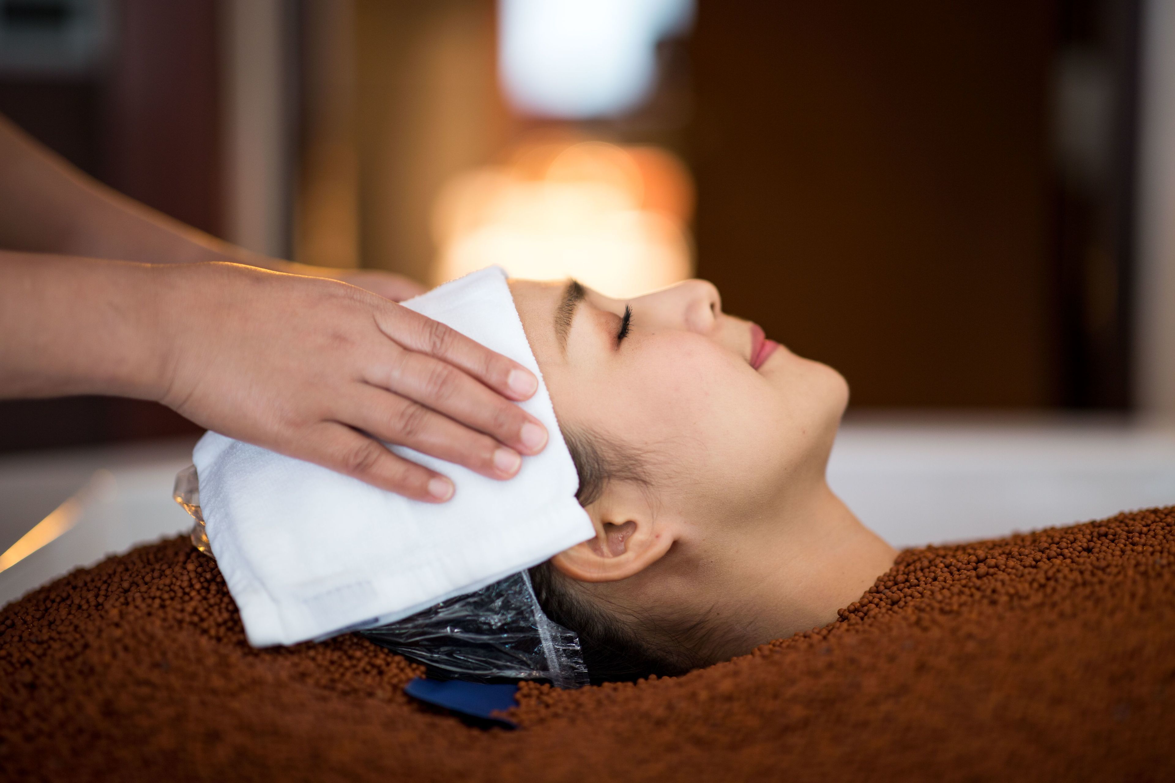A person lying down with a towel over their head, possibly in a spa setting.