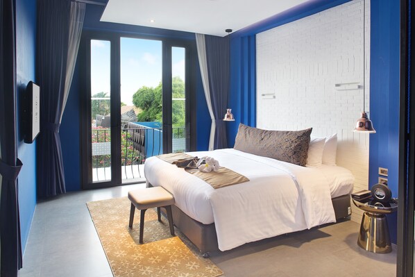 A modern bedroom with a large bed, a bench, a desk, and a view of the outdoors.