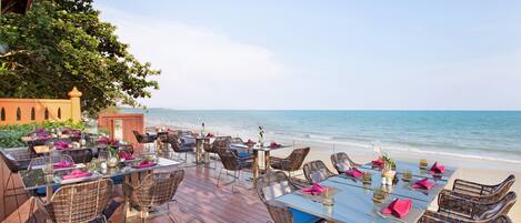Un área de comedor al aire libre con mesas y sillas, con vista a la playa.