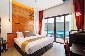 A hotel room with a large bed, a brick accent wall, a balcony with a pool view, and a desk with a chair. - Aksorn Rayong The Vitality Collection (Klaeng)