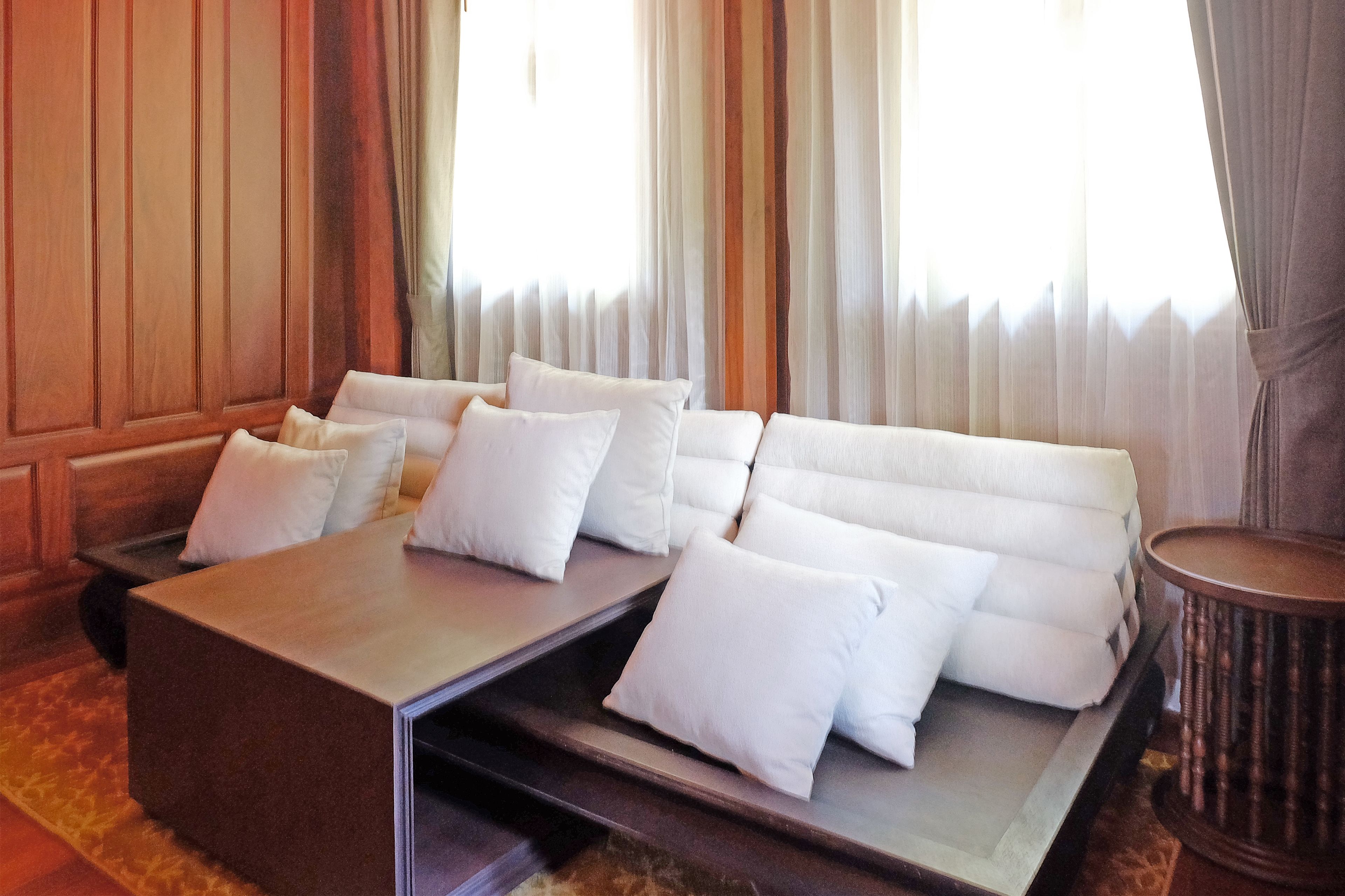 A modern hotel room with a sofa bed, a wooden coffee table, and a small side table.