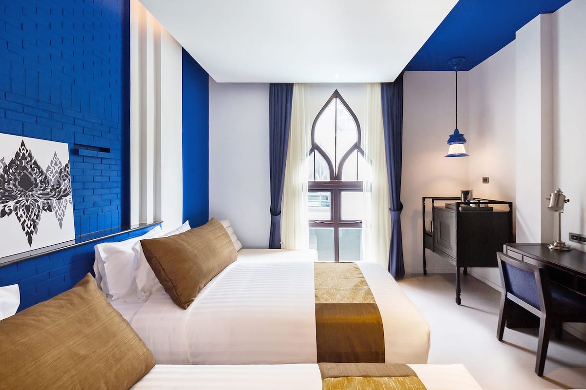 A hotel room with a large bed, a desk, and a chair. There is a window with curtains and a view of the outside.