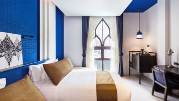 Habitación de hotel con una cama grande, un escritorio y una silla. Se ve una ventana con cortinas y vistas al exterior.