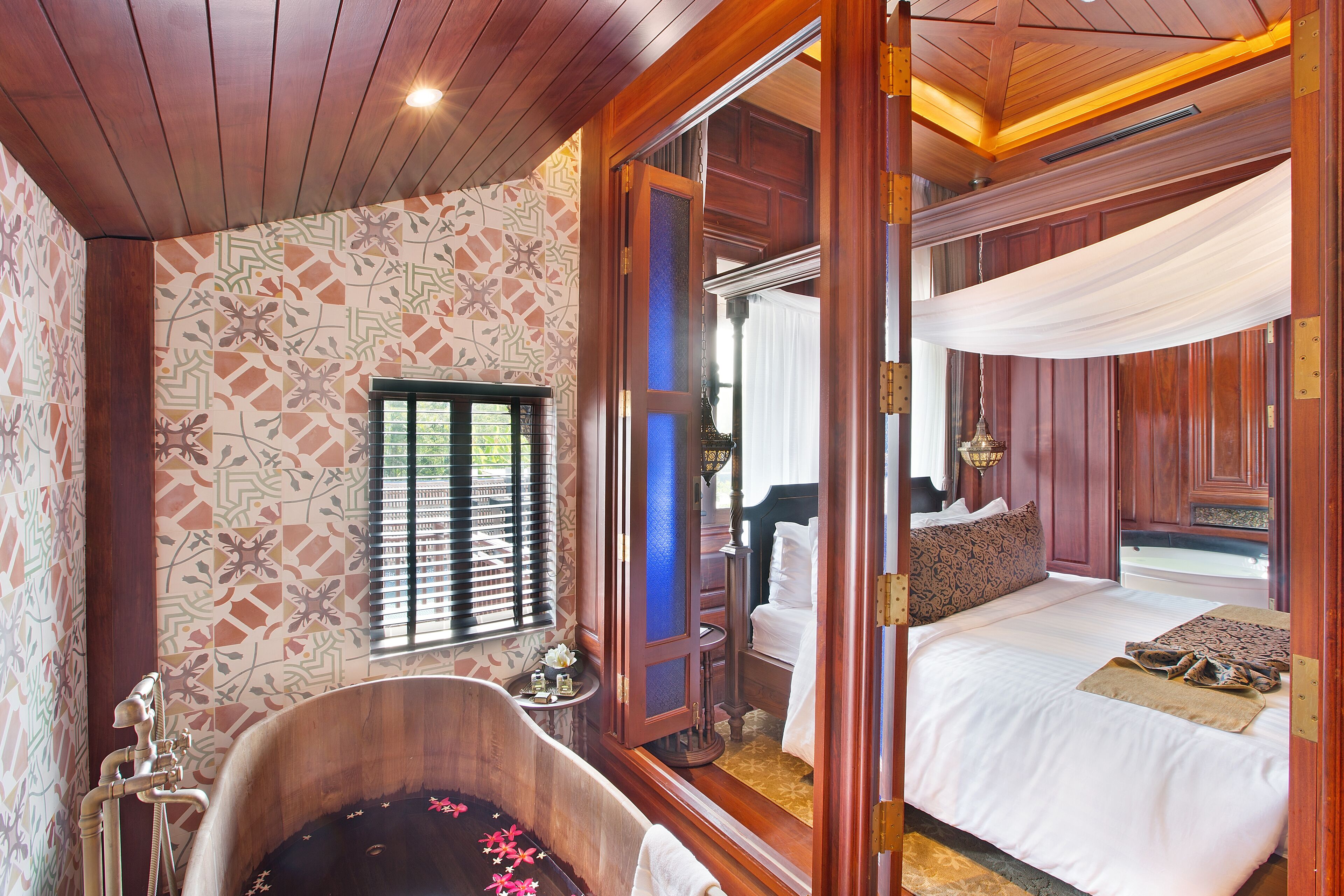 Une pièce avec une baignoire en bois, un lit avec du linge de maison blanc et un mur orné d’un motif.