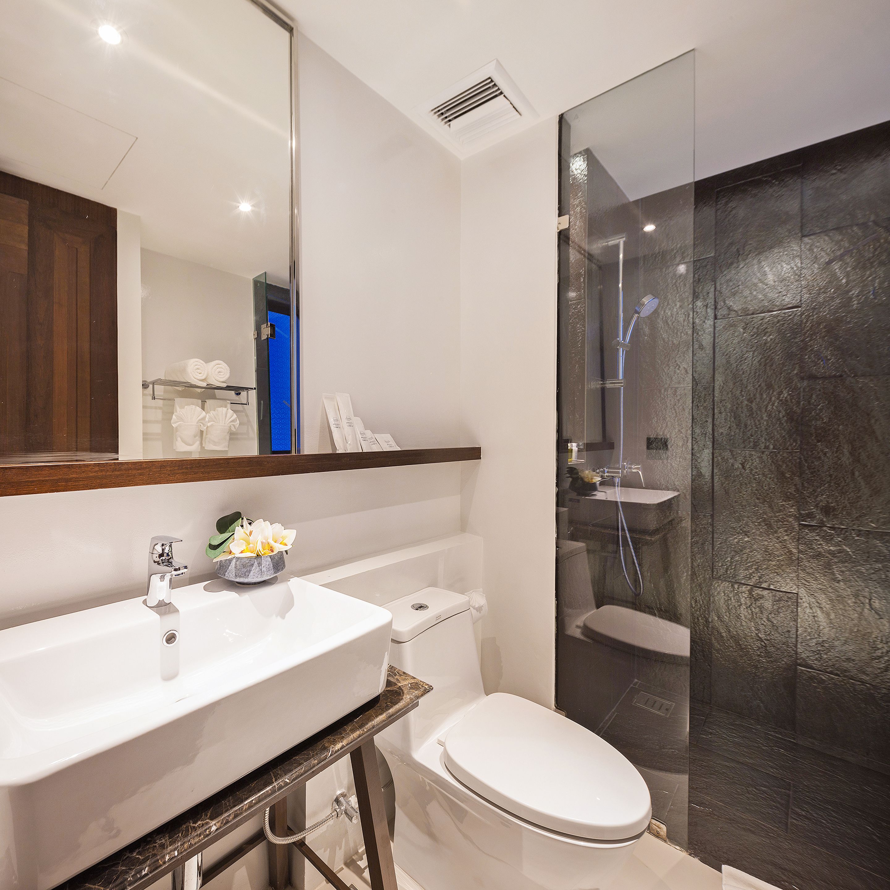 Un baño moderno con un lavamanos blanco, inodoro y zona de ducha con mampara de vidrio.