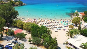 A beach with numerous umbrellas and people. There are cars parked along the road. - Country Home (Kalamata)
