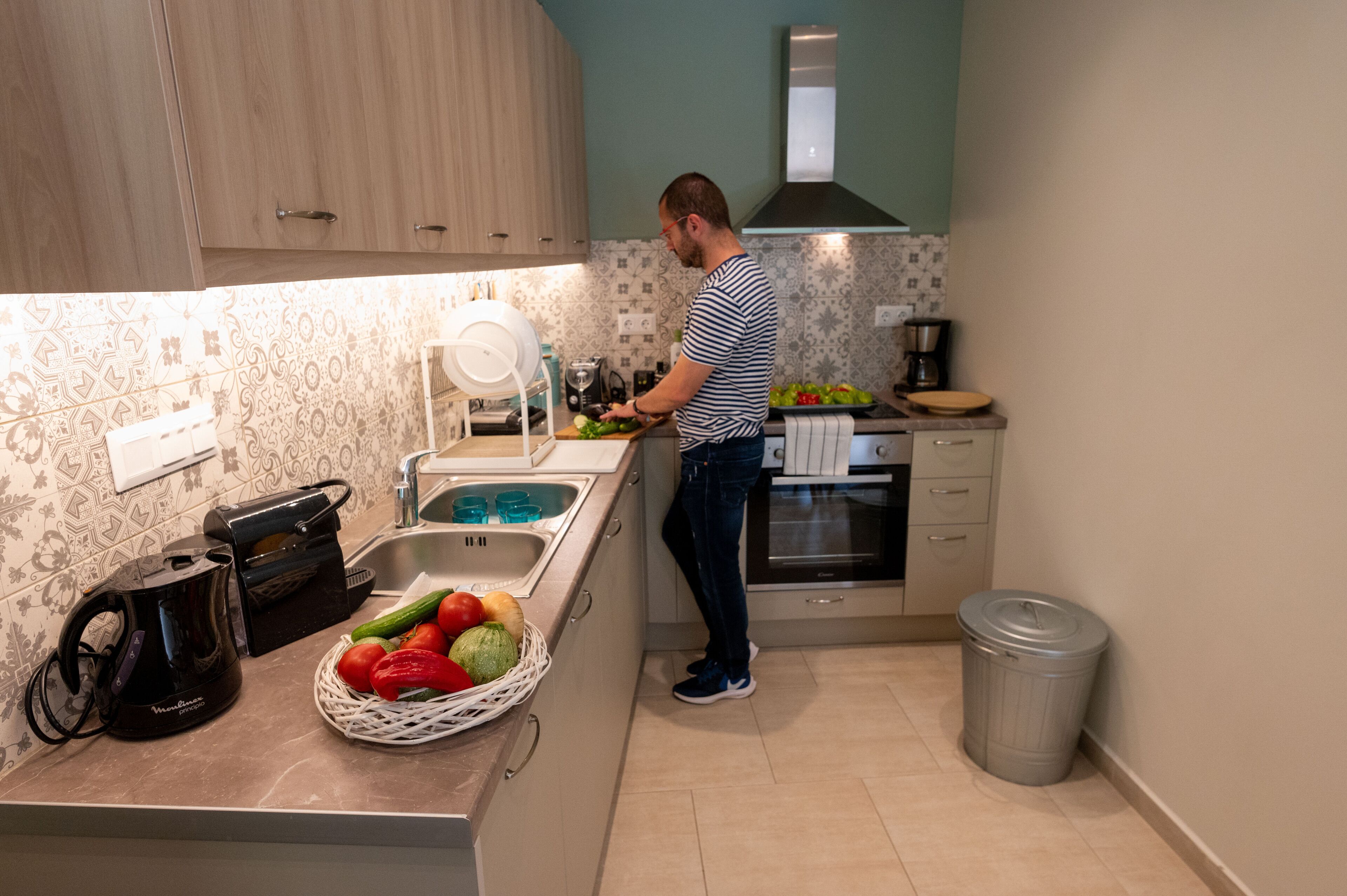 A kitchen with wooden cabinets, a sink, a coffee maker, and a trash can.