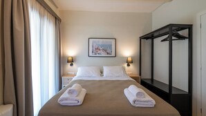 A hotel room with a bed, two bedside tables, a wall-mounted painting, a black wardrobe, and a window with curtains. - Country Home (Kalamata)