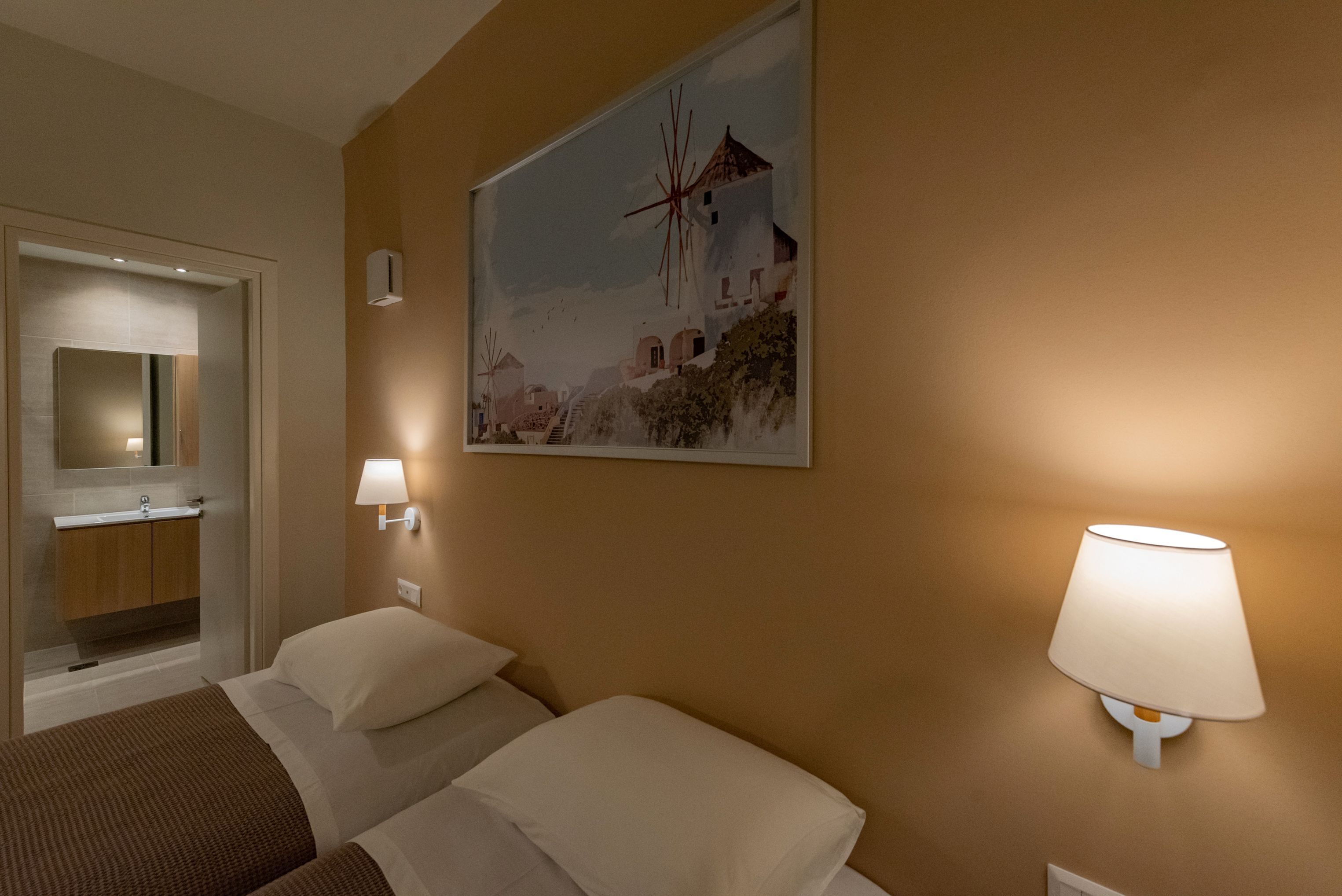 A hotel room with two beds, a bathroom with a sink, and a painting of a windmill on the wall.